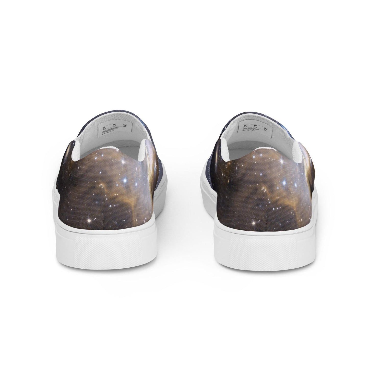 Rear view of a pair of slip-on sneakers featuring a galaxy-themed design with dark cosmic clouds and scattered stars in gold, blue, and black tones. The shoes have white inner linings and white rubber soles, displayed against a clean white background.