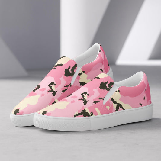 Pair of slip-on canvas shoes with a pink, yellow, and black camouflage pattern, featuring white rubber soles, displayed on a light gray surface with geometric shadows in the background.