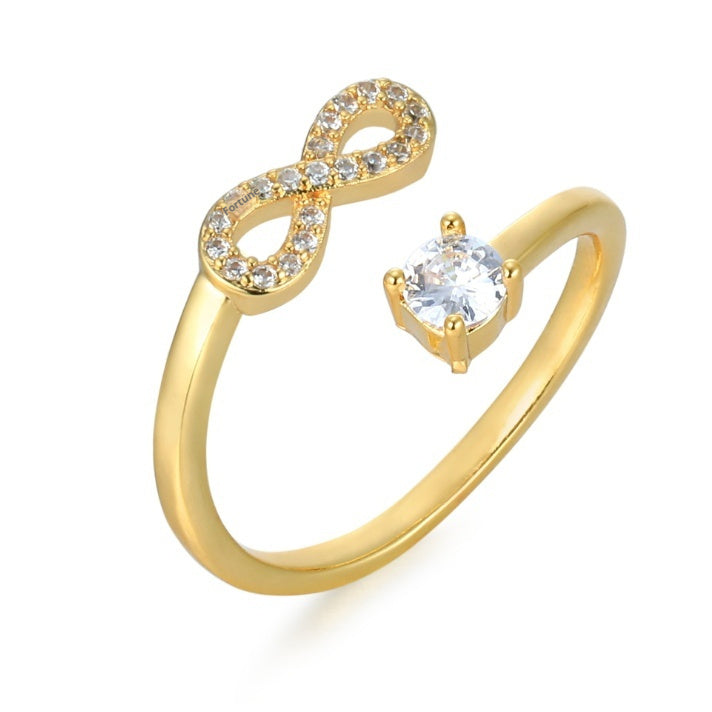 Gold ring with infinity symbol and clear gemstone on a white background
