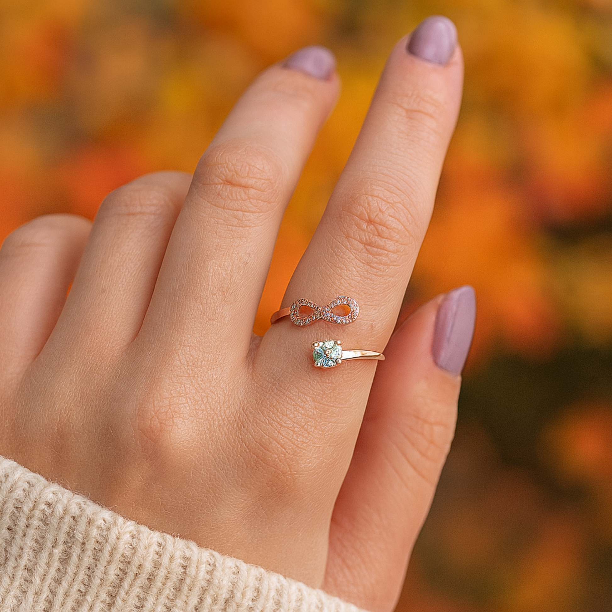Hand wearing a rose gold infinity ring with a blurred autumn background.