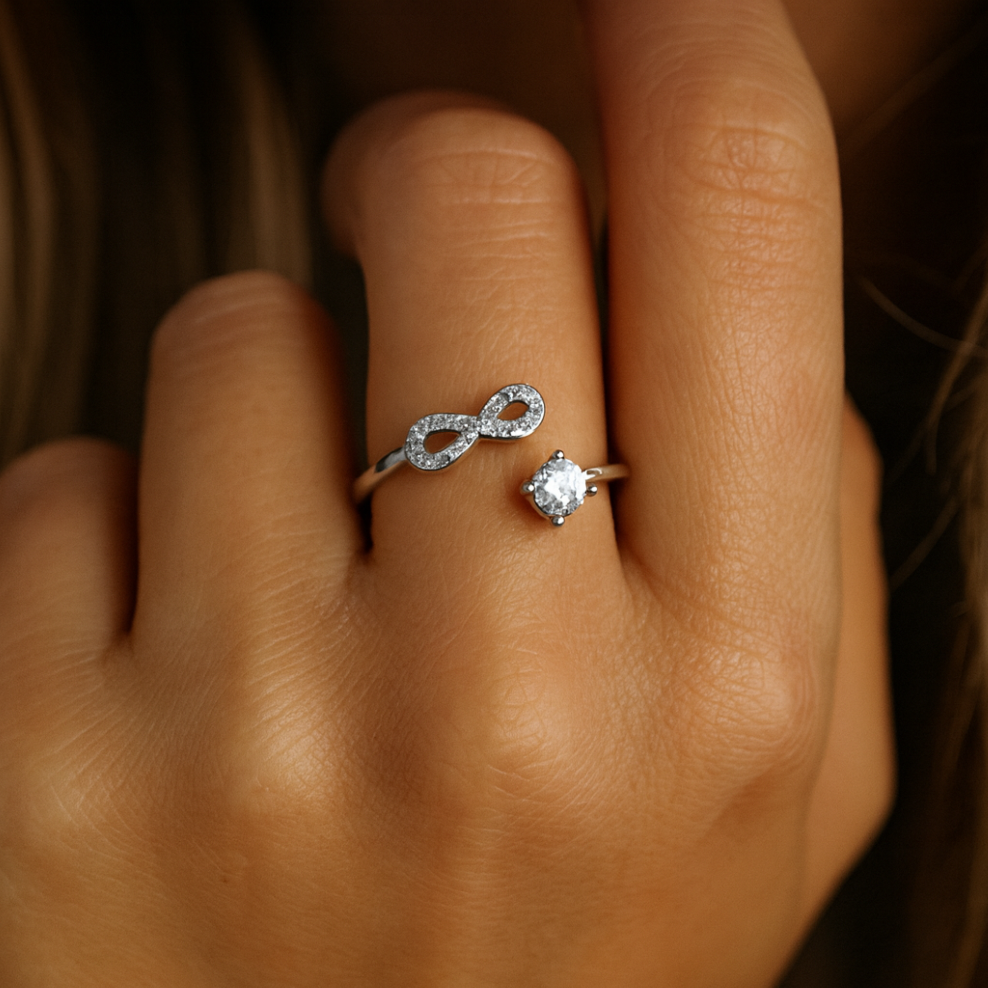 Close-up of a hand wearing an infinity ring with a blurred background.