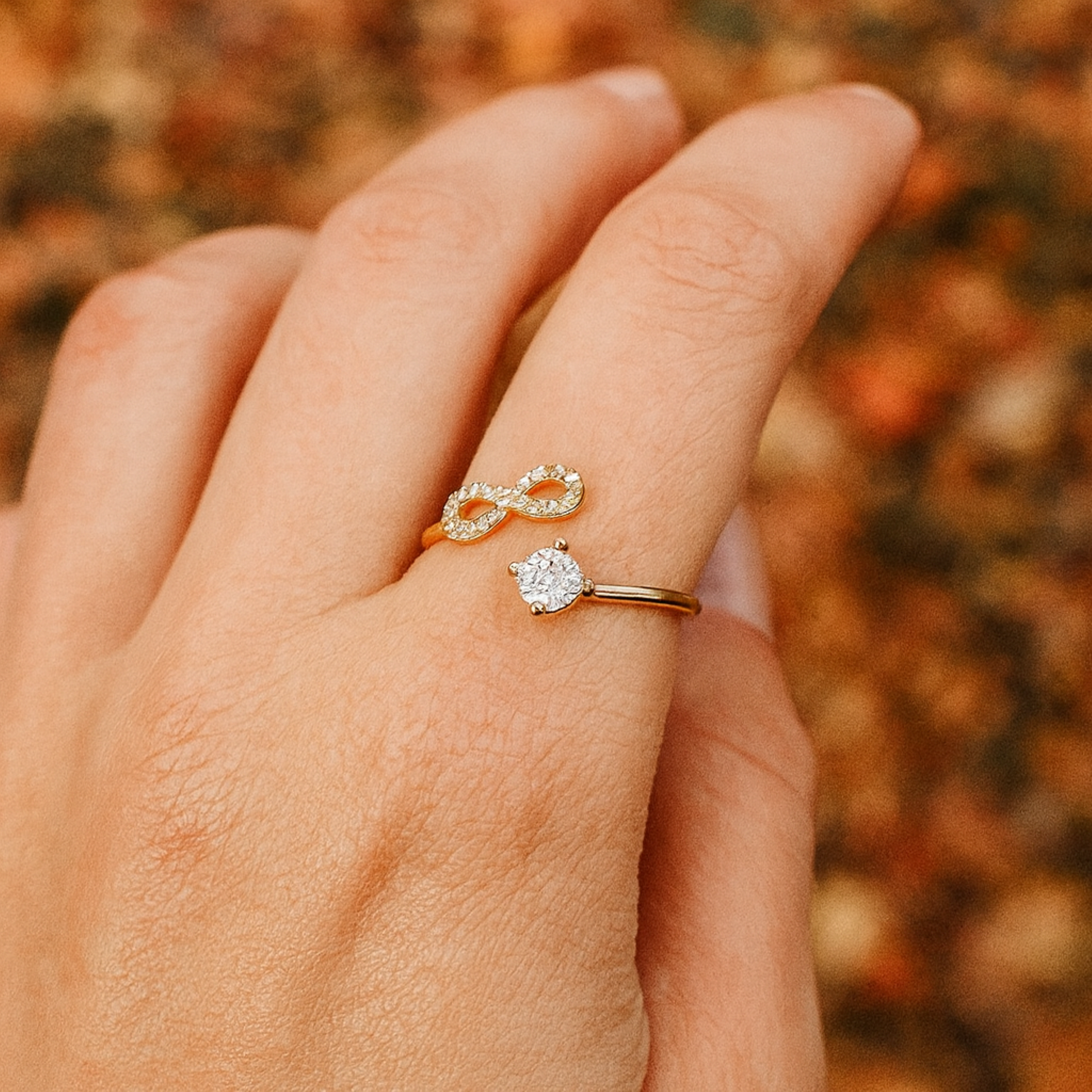 Hand wearing an infinity gold ring with a blurred autumn background