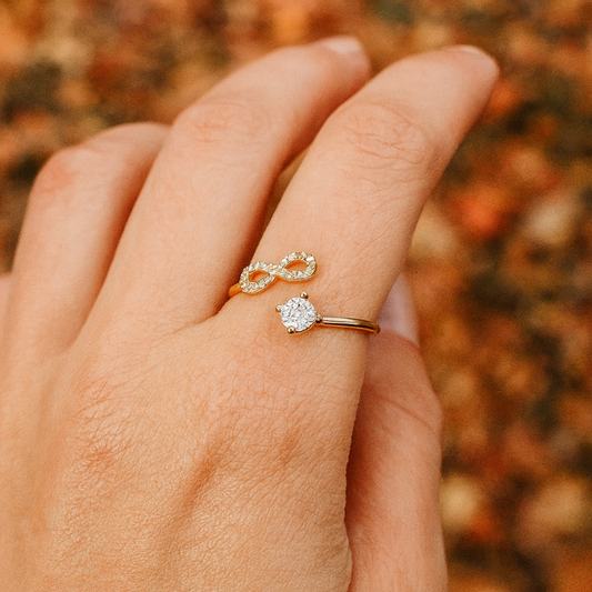 Hand wearing an infinity gold ring with a blurred autumn background