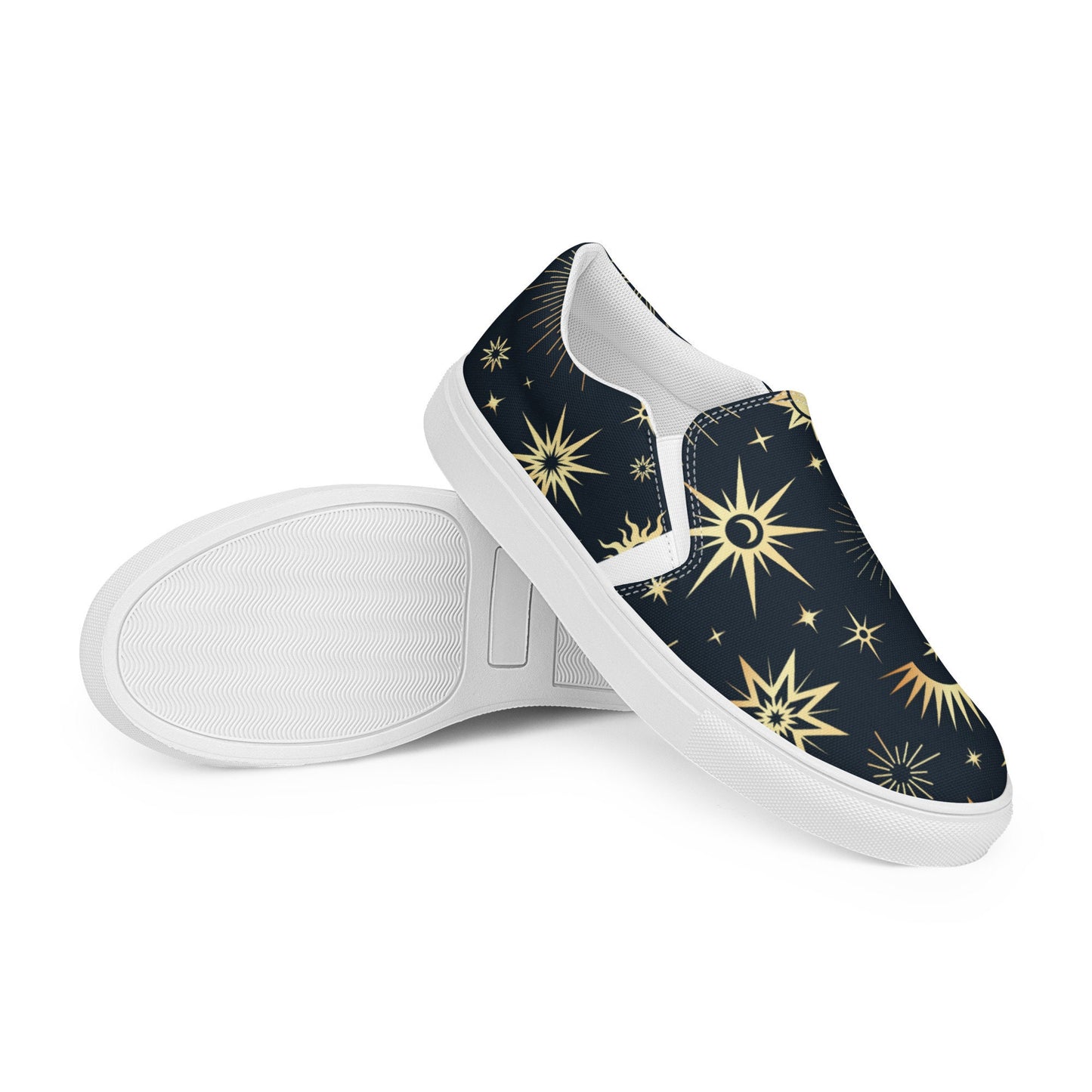 Pair of slip-on canvas shoes featuring a dark navy background with a gold celestial pattern of suns, stars, and crescent moons. One shoe is positioned upright while the other is laid on its side to show the textured white rubber sole. Displayed on a white background.