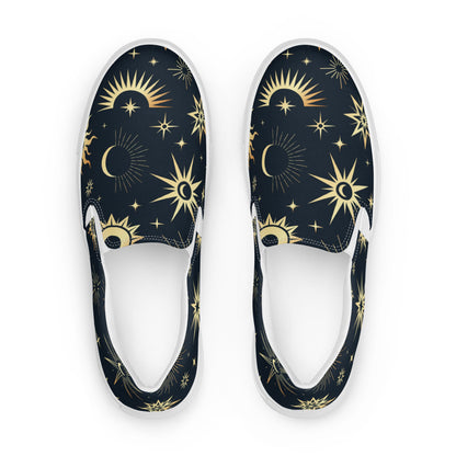 Top-down view of a pair of slip-on canvas shoes featuring a dark navy background with a celestial pattern of gold suns, stars, and crescent moons. The shoes have white interiors and white rubber soles, displayed on a clean white background.