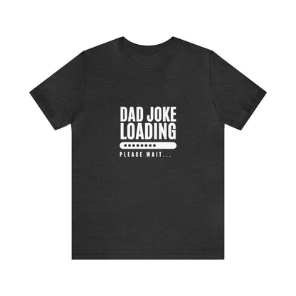 Dark heather gray unisex T-shirt featuring the humorous phrase “Dad Joke Loading, Please Wait…” in bold white letters with a progress bar graphic centered on the front.