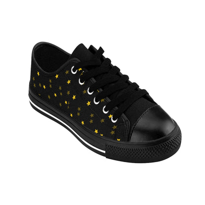 A single black low-top sneaker is shown on a white background. The shoe features black laces, a black rubber toe cap, and a black sole with a white stripe. The canvas upper is decorated with a scattered pattern of small gold stars, creating a celestial, night-sky-inspired design.