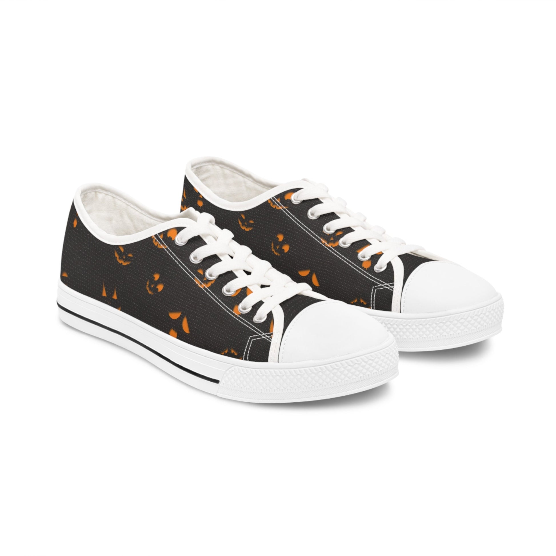 Halloween-themed women&#39;s low-top canvas sneakers with spooky orange jack-o&#39;-lantern face pattern on a black background, featuring white laces, white rubber toe caps, and soles – stylish fall holiday shoes perfect for Halloween parties, casual October outfits, and spooky season fashion.
