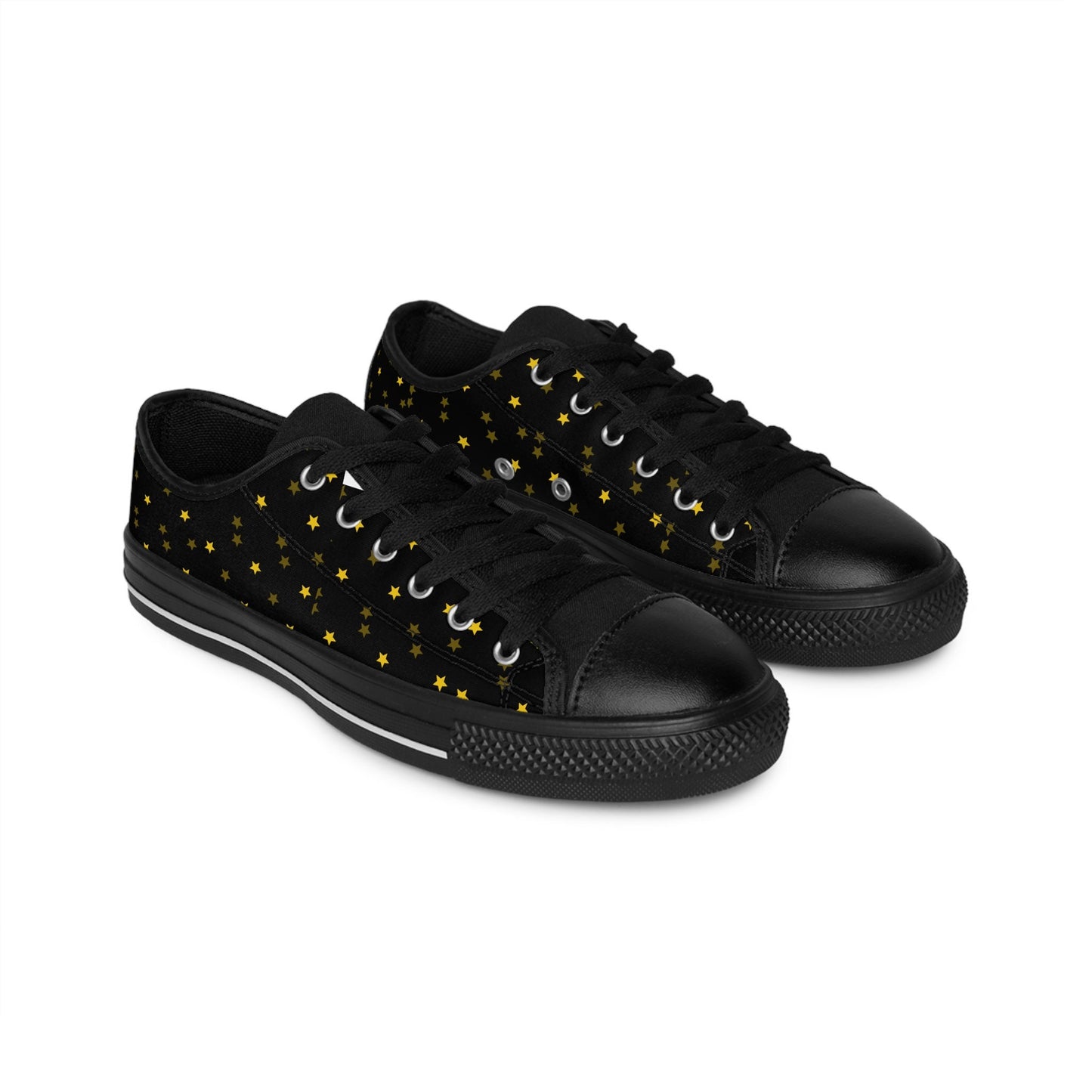 A pair of black low-top canvas sneakers with black laces and rubber soles is shown on a white background. The shoes feature a celestial pattern of small yellow stars scattered across the sides, giving them a whimsical, night-sky-inspired design.