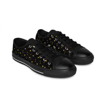 A pair of black low-top canvas sneakers with black laces and rubber soles is shown on a white background. The shoes feature a celestial pattern of small yellow stars scattered across the sides, giving them a whimsical, night-sky-inspired design.