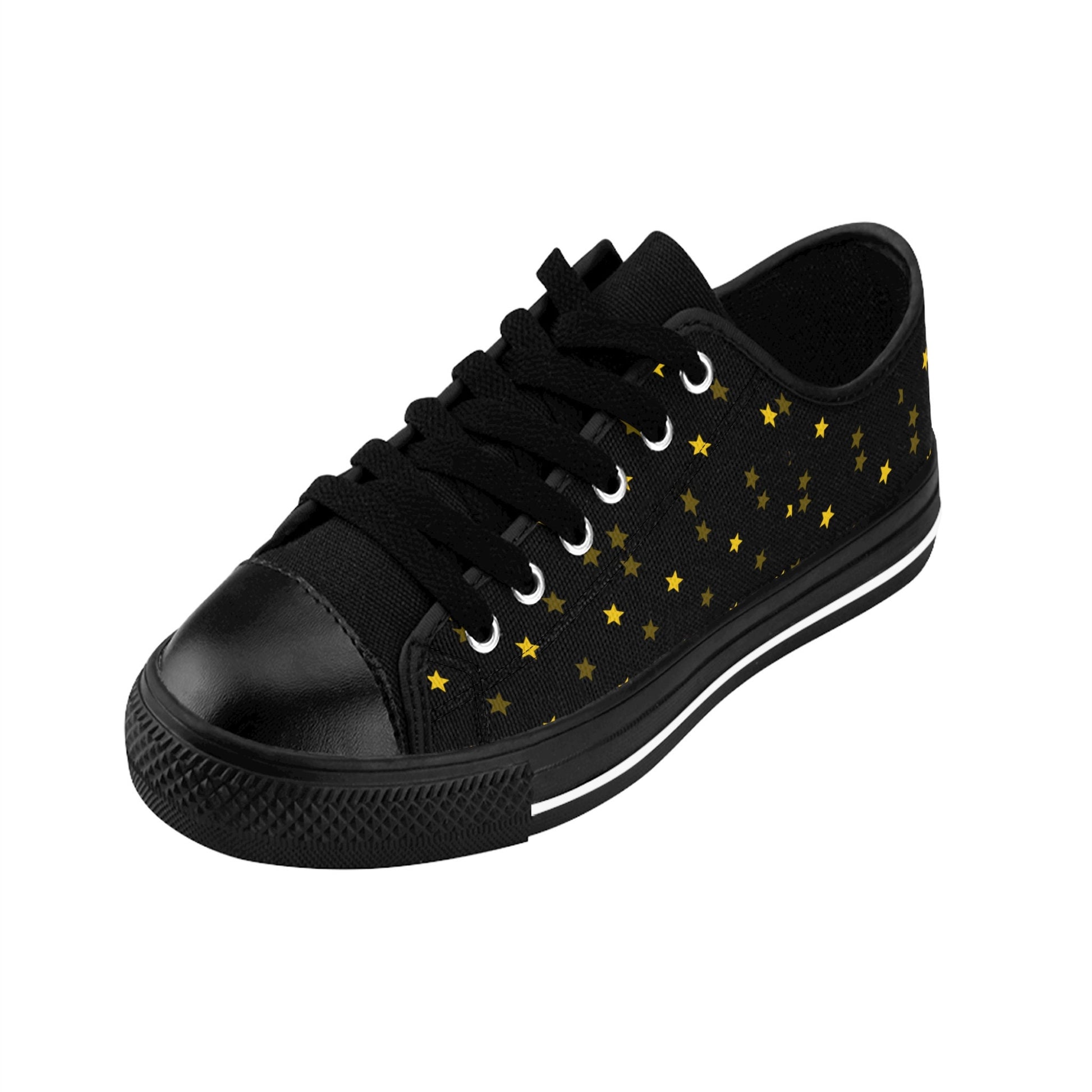 A single black low-top sneaker is displayed on a white background. The shoe features black laces, a black rubber toe cap, and a black sole with a white stripe. Its canvas upper is adorned with a scattered pattern of small yellow and gold stars, giving it a celestial, night-sky theme.