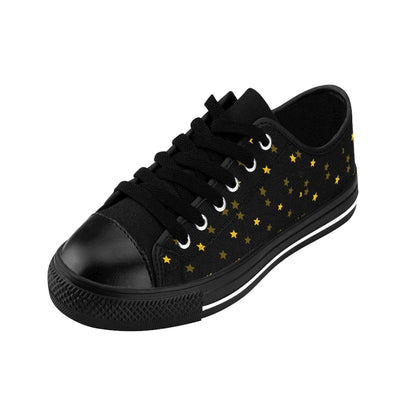 A single black low-top sneaker is displayed on a white background. The shoe features black laces, a black rubber toe cap, and a black sole with a white stripe. Its canvas upper is adorned with a scattered pattern of small yellow and gold stars, giving it a celestial, night-sky theme.