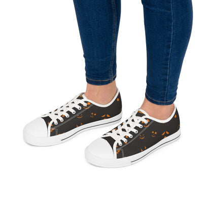 Women&#39;s Halloween low-top canvas sneakers with white laces and rubber soles, featuring a spooky jack-o&#39;-lantern face pattern on a black background – stylish and comfortable fall shoes perfect for October outfits, trick-or-treating, and Halloween parties, modeled with skinny jeans for casual seasonal fashion.