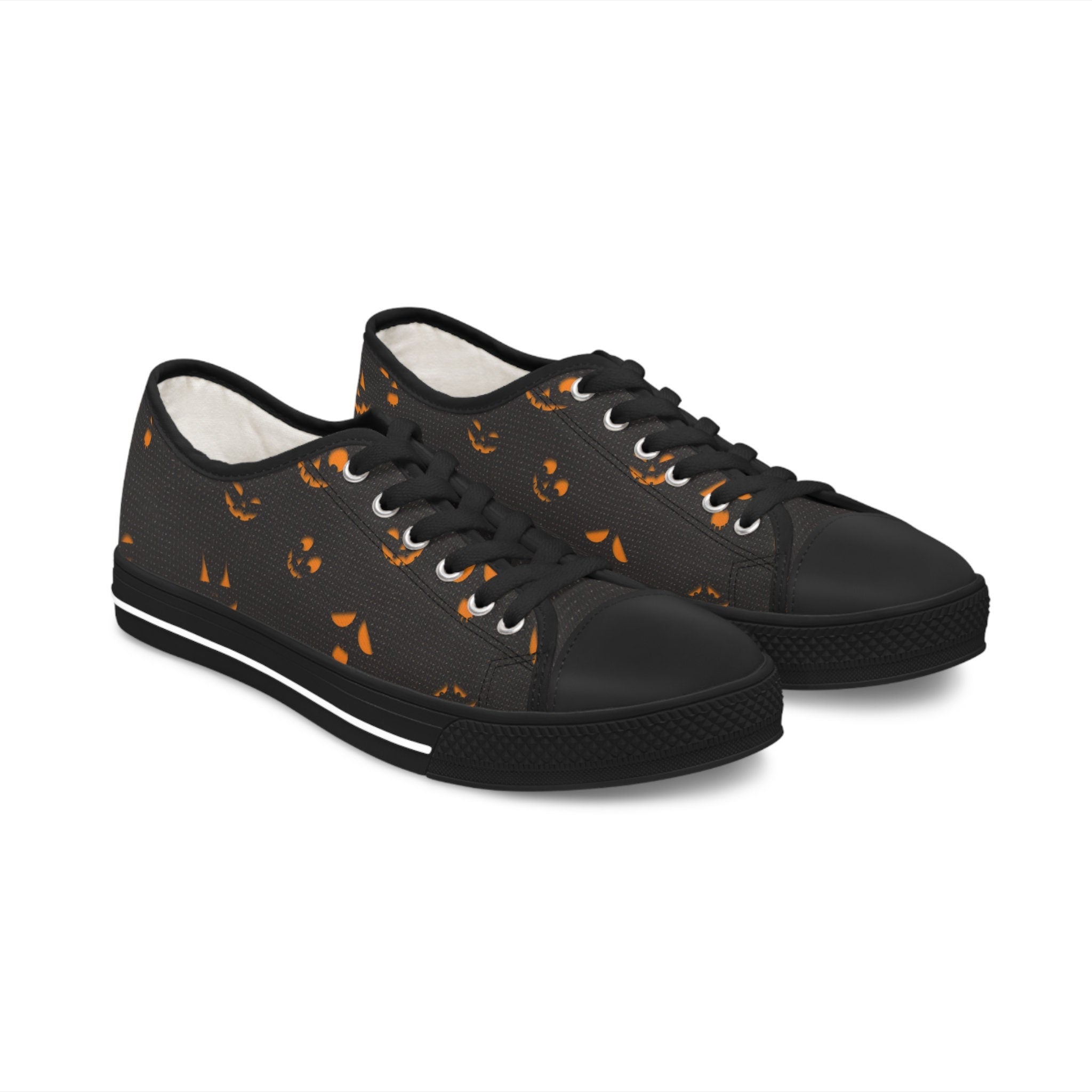 Spooky Halloween low-top canvas sneakers featuring a black background with glowing orange jack-o&#39;-lantern face print, black rubber soles, black laces, and metal eyelets – gothic fall footwear perfect for Halloween costumes, October streetwear, trick-or-treat nights, and festive seasonal style.