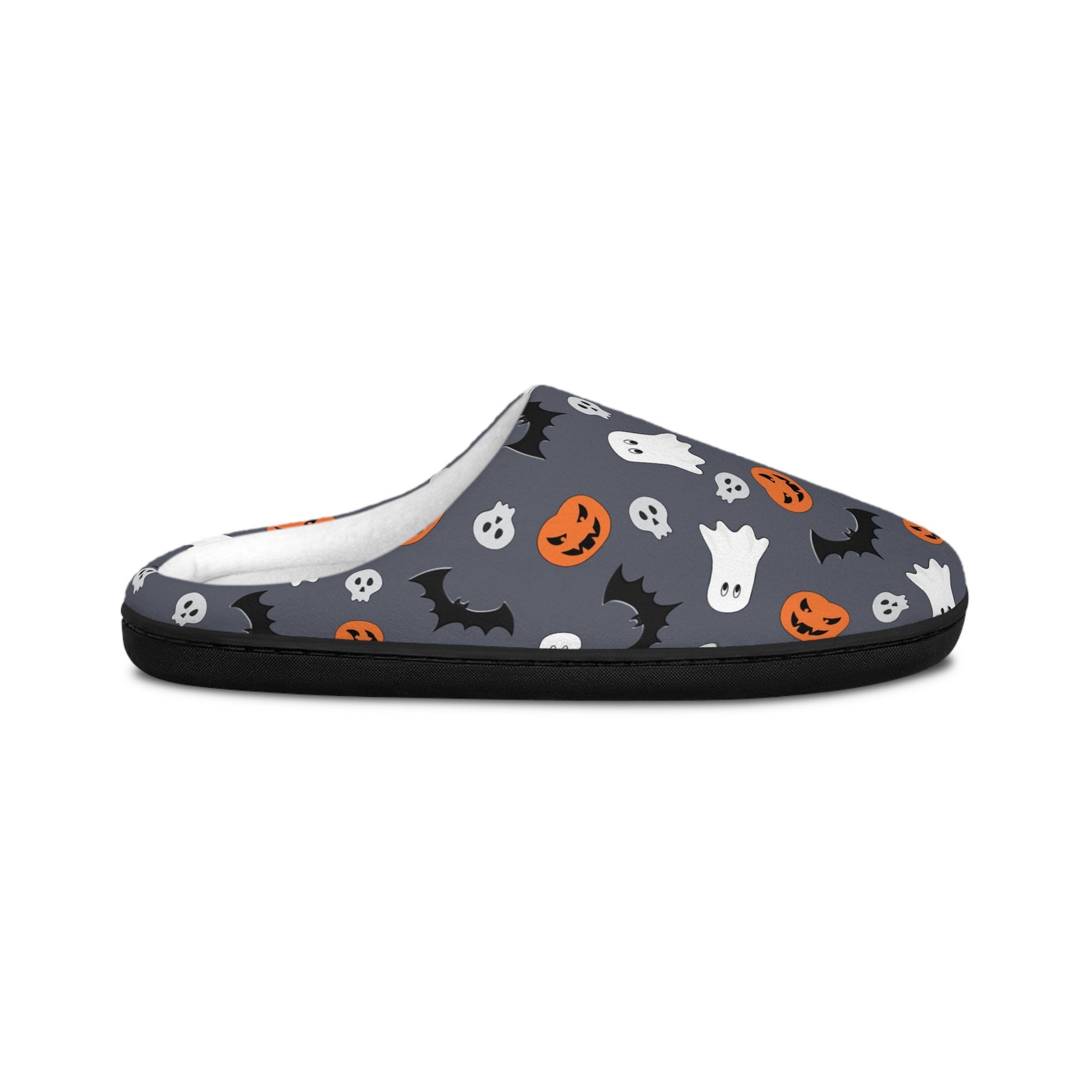 Side view of a Halloween-themed slipper with a dark gray background, decorated with a playful pattern of white ghosts, black bats, orange jack-o&#39;-lanterns, and small skulls. The slipper features a soft white interior lining and a black sole, shown against a white background.