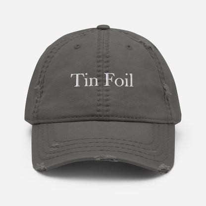 A gray distressed baseball cap with the words &quot;Tin Foil&quot; embroidered in white on the front. The cap features frayed detailing and worn patches on the brim and crown seams, giving it a vintage, well-loved appearance. It is shown against a clean white background, centered and facing forward.
