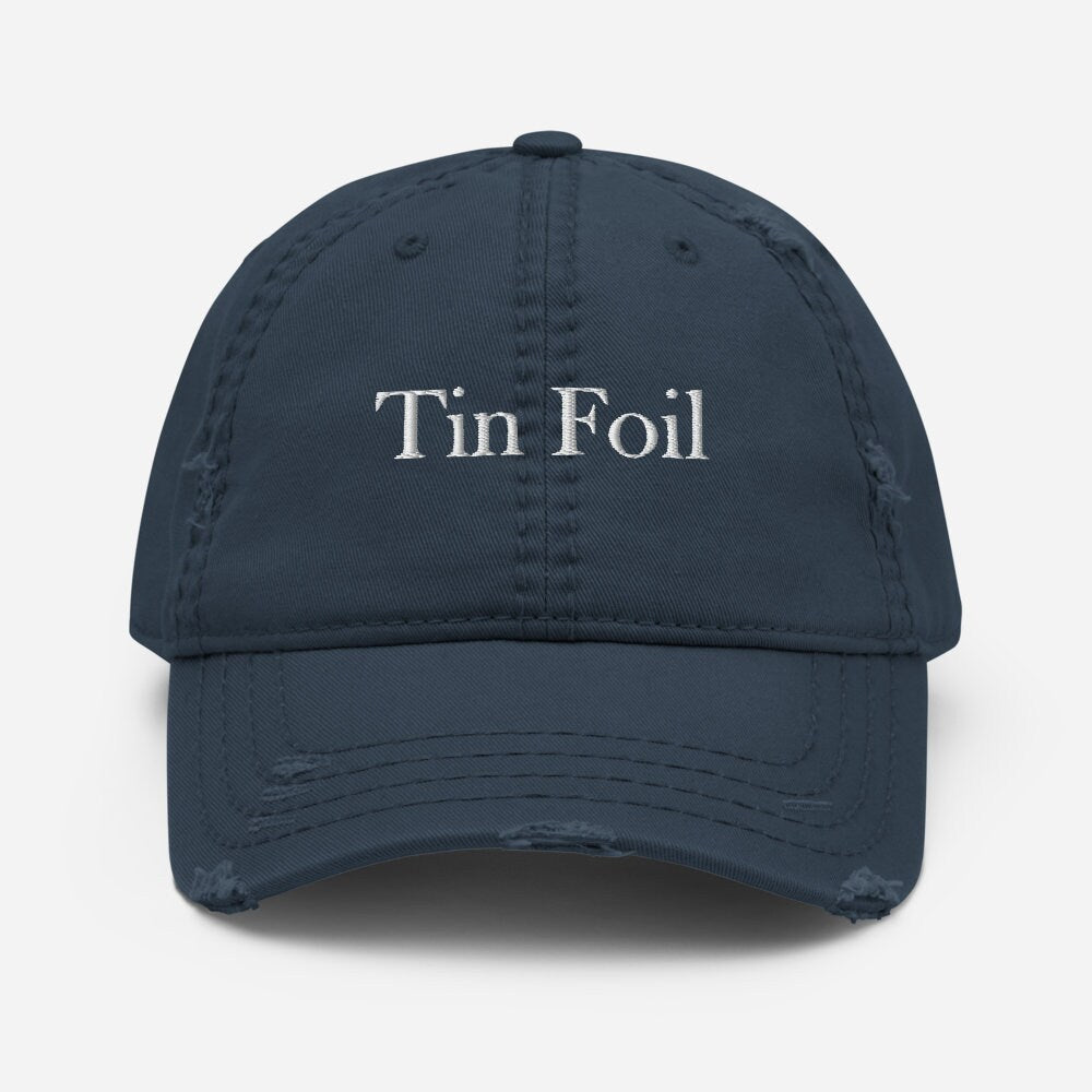 A navy blue distressed baseball cap with the words &quot;Tin Foil&quot; embroidered in white on the front. The cap has frayed edges and worn detailing along the brim and seams, giving it a vintage, lived-in look. It is displayed against a plain white background, centered and facing forward.