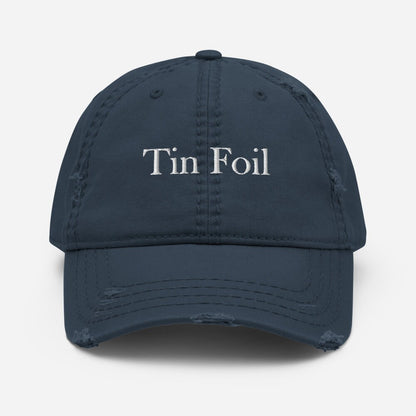 A navy blue distressed baseball cap with the words &quot;Tin Foil&quot; embroidered in white on the front. The cap has frayed edges and worn detailing along the brim and seams, giving it a vintage, lived-in look. It is displayed against a plain white background, centered and facing forward.