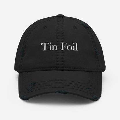 A black distressed baseball cap with the words &quot;Tin Foil&quot; embroidered in white on the front. The hat features intentional fraying and worn details along the brim and crown seams, giving it a vintage, rugged look. The cap is displayed against a plain white background, centered and facing forward.