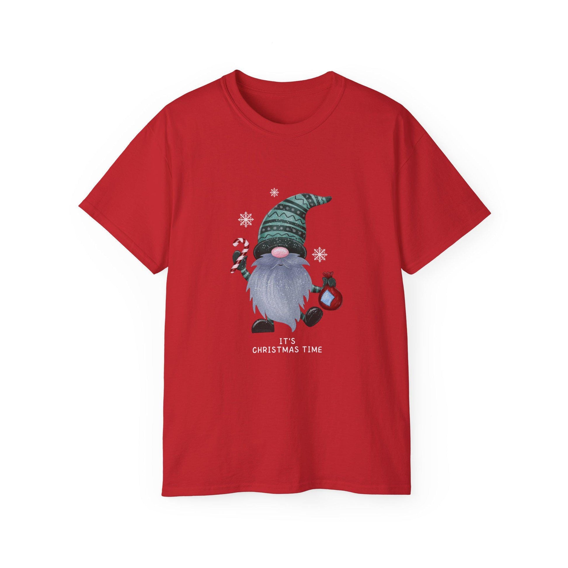 A red unisex T-shirt is displayed against a white background, featuring a festive graphic of a Christmas gnome with a long gray beard, wearing a green patterned hat. The gnome is holding a candy cane and a red ornament, surrounded by white snowflakes. Below the illustration, the text &quot;It&#39;s Christmas Time&quot; is printed in white. The shirt has a classic crew neck and short sleeves.