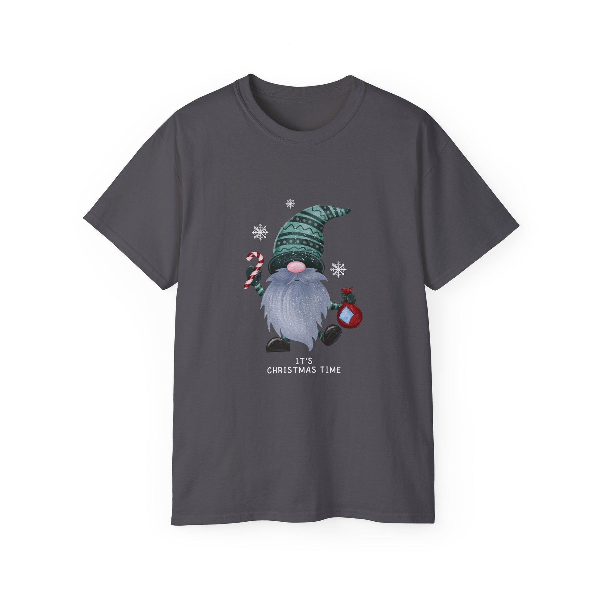 A charcoal gray unisex T-shirt is shown against a white background, featuring a whimsical Christmas gnome graphic. The gnome has a long gray beard, a pink nose, and wears a patterned green hat. He holds a red and white candy cane in one hand and a red ornament in the other, surrounded by white snowflakes. The phrase &quot;It&#39;s Christmas Time&quot; is printed below the illustration in white text. The shirt has a classic crew neck and short sleeves.