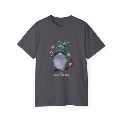 A charcoal gray unisex T-shirt is shown against a white background, featuring a whimsical Christmas gnome graphic. The gnome has a long gray beard, a pink nose, and wears a patterned green hat. He holds a red and white candy cane in one hand and a red ornament in the other, surrounded by white snowflakes. The phrase &quot;It&#39;s Christmas Time&quot; is printed below the illustration in white text. The shirt has a classic crew neck and short sleeves.