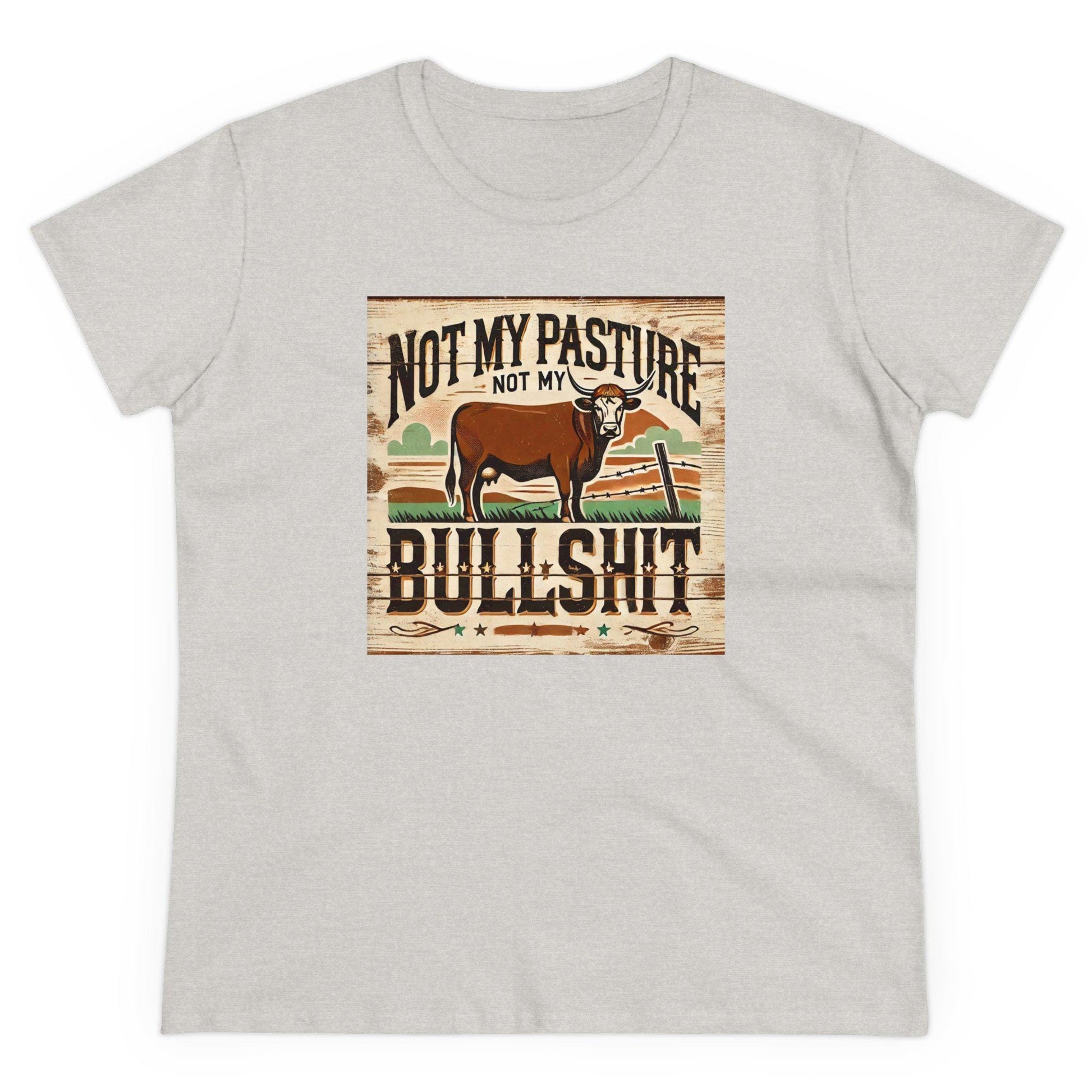 A light gray T-shirt is displayed flat against a white background. The shirt features a rustic, vintage-style graphic of a brown cow standing in a western field with a broken fence. Above and below the image, bold distressed text reads: &quot;Not my pasture, not my bullshit.&quot; The design has a country, farmhouse aesthetic with earthy tones and a wooden plank-style background.