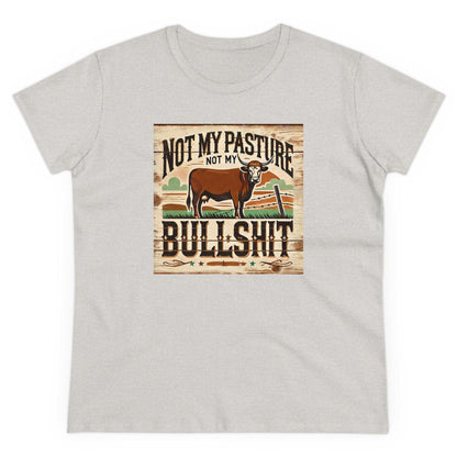 A light gray T-shirt is displayed flat against a white background. The shirt features a rustic, vintage-style graphic of a brown cow standing in a western field with a broken fence. Above and below the image, bold distressed text reads: &quot;Not my pasture, not my bullshit.&quot; The design has a country, farmhouse aesthetic with earthy tones and a wooden plank-style background.