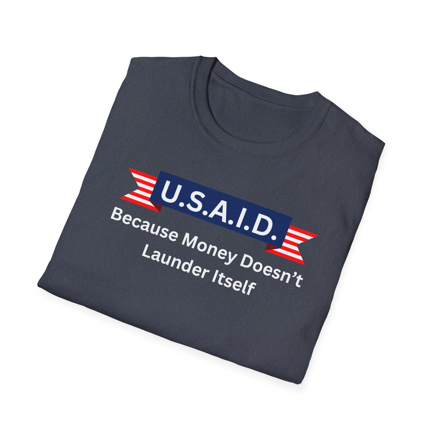 A folded navy blue T-shirt is displayed on a white background. The shirt features a bold satirical design with a navy blue banner labeled &quot;U.S.A.I.D.&quot; in white letters, accented by red and white striped ribbon graphics on either side. Below the banner, the white text reads: &quot;Because Money Doesn’t Launder Itself.&quot; The design mimics a government agency logo with a humorous political commentary.