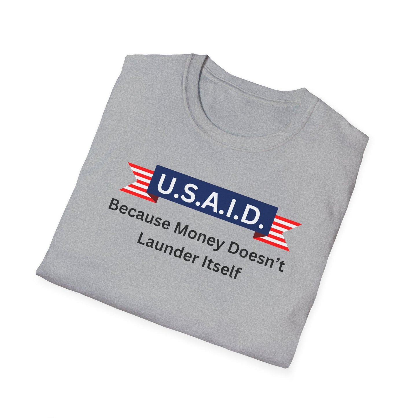 A light gray T-shirt is neatly folded on a white background. The shirt features a bold, satirical graphic with a navy blue banner labeled &quot;U.S.A.I.D.&quot; in white text, flanked by red and white striped ribbon designs. Beneath the banner, black text reads: &quot;Because Money Doesn’t Launder Itself.&quot; The design parodies a government agency logo with a humorous political message.