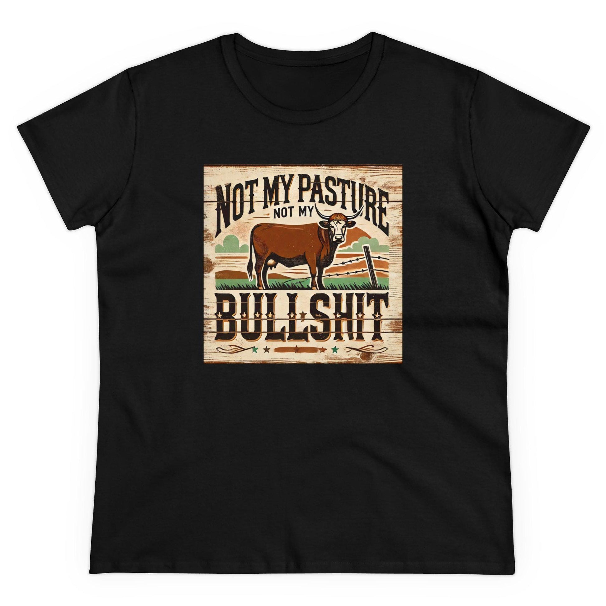 A black T-shirt is laid flat against a white background, featuring a bold, rustic-style graphic on the front. The design includes a brown cow standing in a western landscape with a wooden fence and grassy field. Above and below the cow, the text reads: &quot;Not my pasture, not my bullshit&quot; in distressed, western-style lettering. The overall design has a vintage, country-inspired aesthetic.