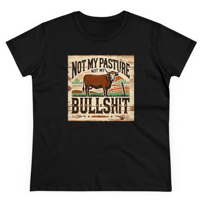 A black T-shirt is laid flat against a white background, featuring a bold, rustic-style graphic on the front. The design includes a brown cow standing in a western landscape with a wooden fence and grassy field. Above and below the cow, the text reads: &quot;Not my pasture, not my bullshit&quot; in distressed, western-style lettering. The overall design has a vintage, country-inspired aesthetic.