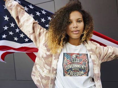 Confident woman wearing white &#39;Less Government More Freedom&#39; patriotic t-shirt and camouflage jacket while holding American flag — bold conservative fashion celebrating liberty and independence.