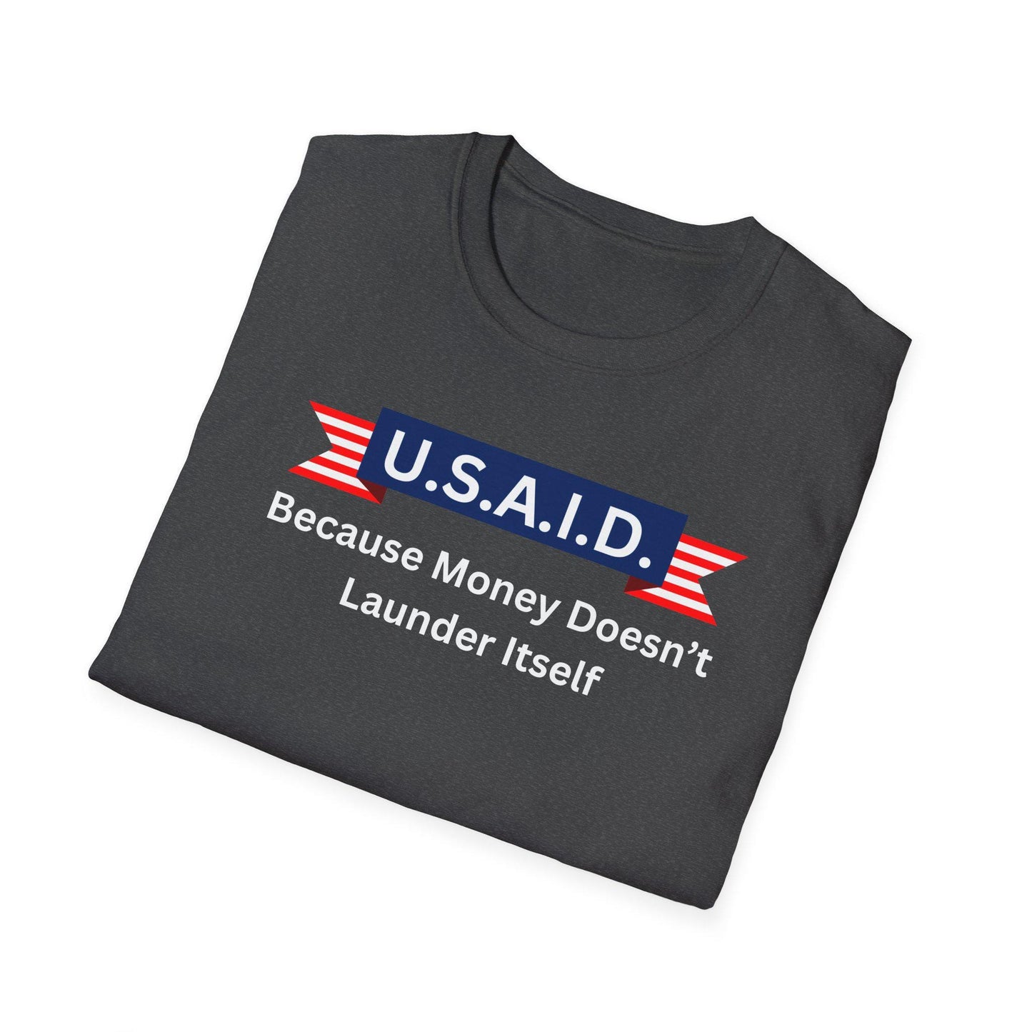 A dark charcoal gray T-shirt is neatly folded on a white background. The shirt features a satirical design with a navy blue banner reading &quot;U.S.A.I.D.&quot; in white letters, flanked by red and white striped ribbon graphics. Beneath the banner, white text states: &quot;Because Money Doesn’t Launder Itself.&quot; The design mimics a government agency logo with a humorous political twist.