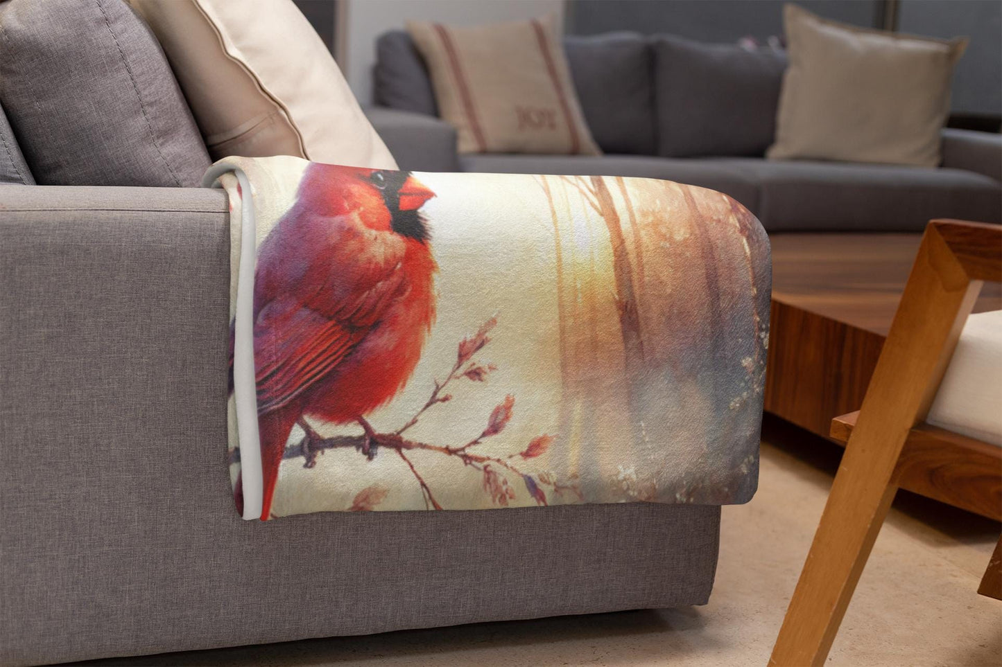 Cozy blanket with a vibrant red cardinal design draped over the arm of a gray sofa in a modern living room with neutral-toned décor.