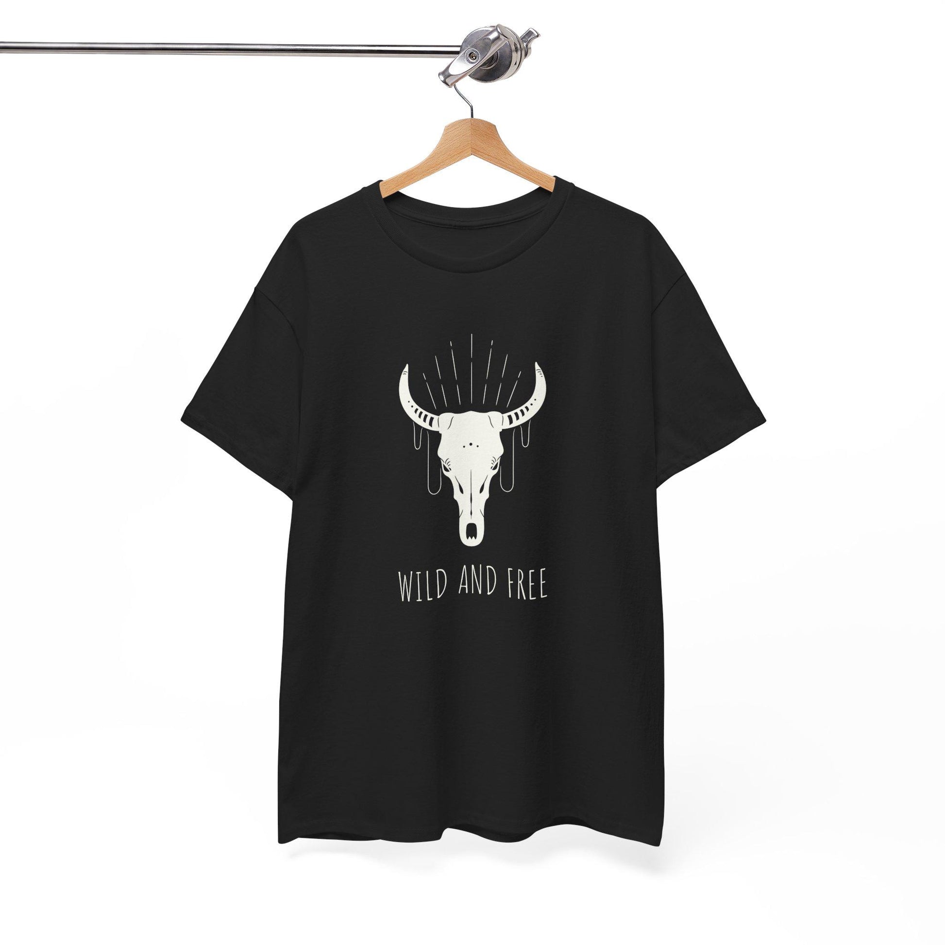 Black T-shirt hanging on a wooden hanger against a plain white background. The shirt features a graphic of a white bull skull with decorative lines above it and the text “WILD AND FREE” below.