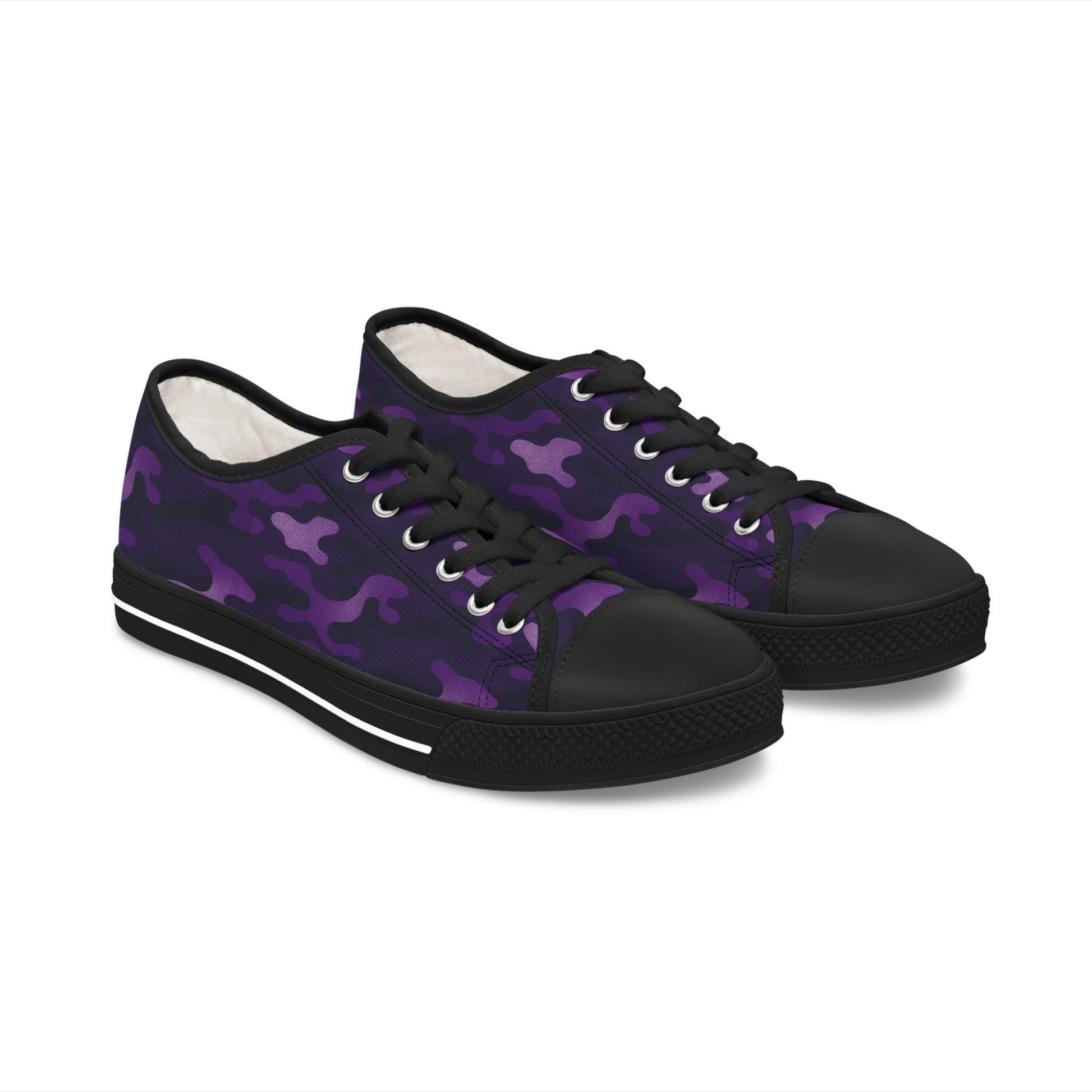 A pair of low-top canvas sneakers featuring a vibrant purple camouflage pattern with black and violet accents. The shoes are styled with black rubber soles, black toe caps, and black laces, giving them a bold, edgy look.