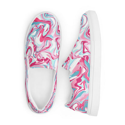 A pair of slip-on canvas sneakers displayed from a top-down view on a white background. The shoes feature a bold marbled swirl pattern in vibrant shades of pink, turquoise, and white, with white elastic side panels and white rubber soles. One shoe is positioned upright while the other lies flat, showcasing both the top and side design.