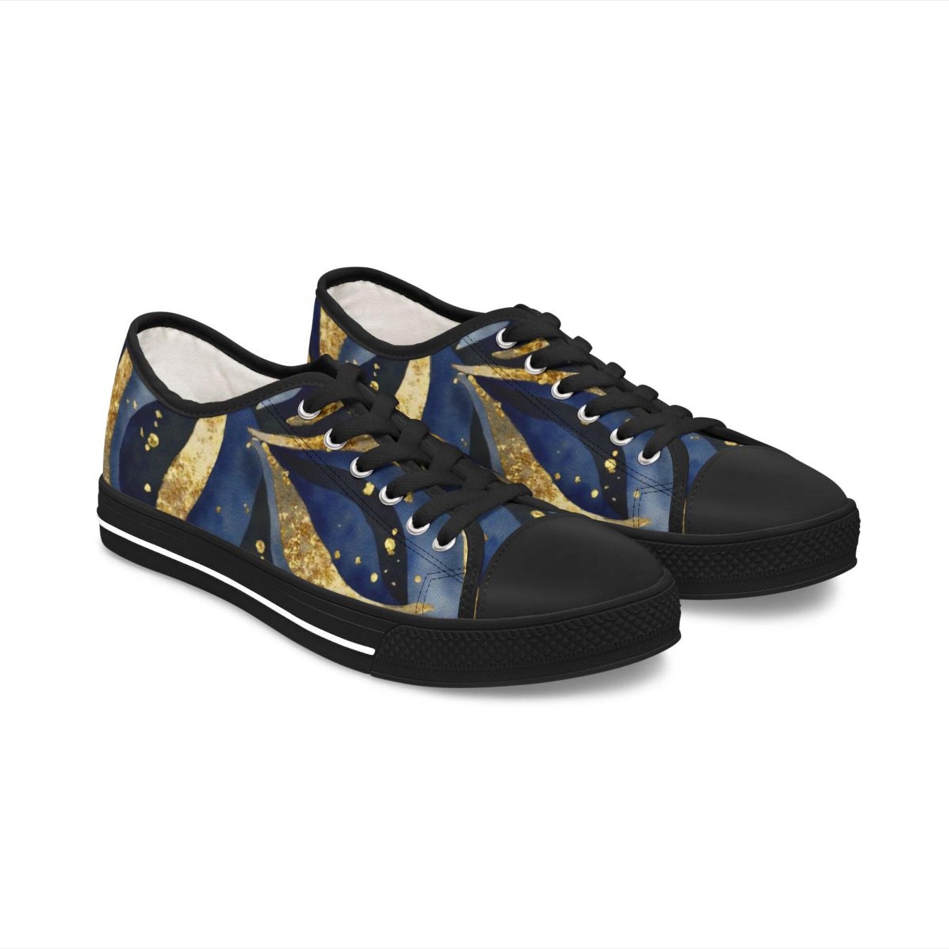 A pair of low-top canvas sneakers with black soles, black laces, and black toe caps. The shoe design features an abstract celestial pattern in deep blue and gold tones, resembling shooting stars or comet trails. The background is plain white, highlighting the bold, artistic style of the footwear.