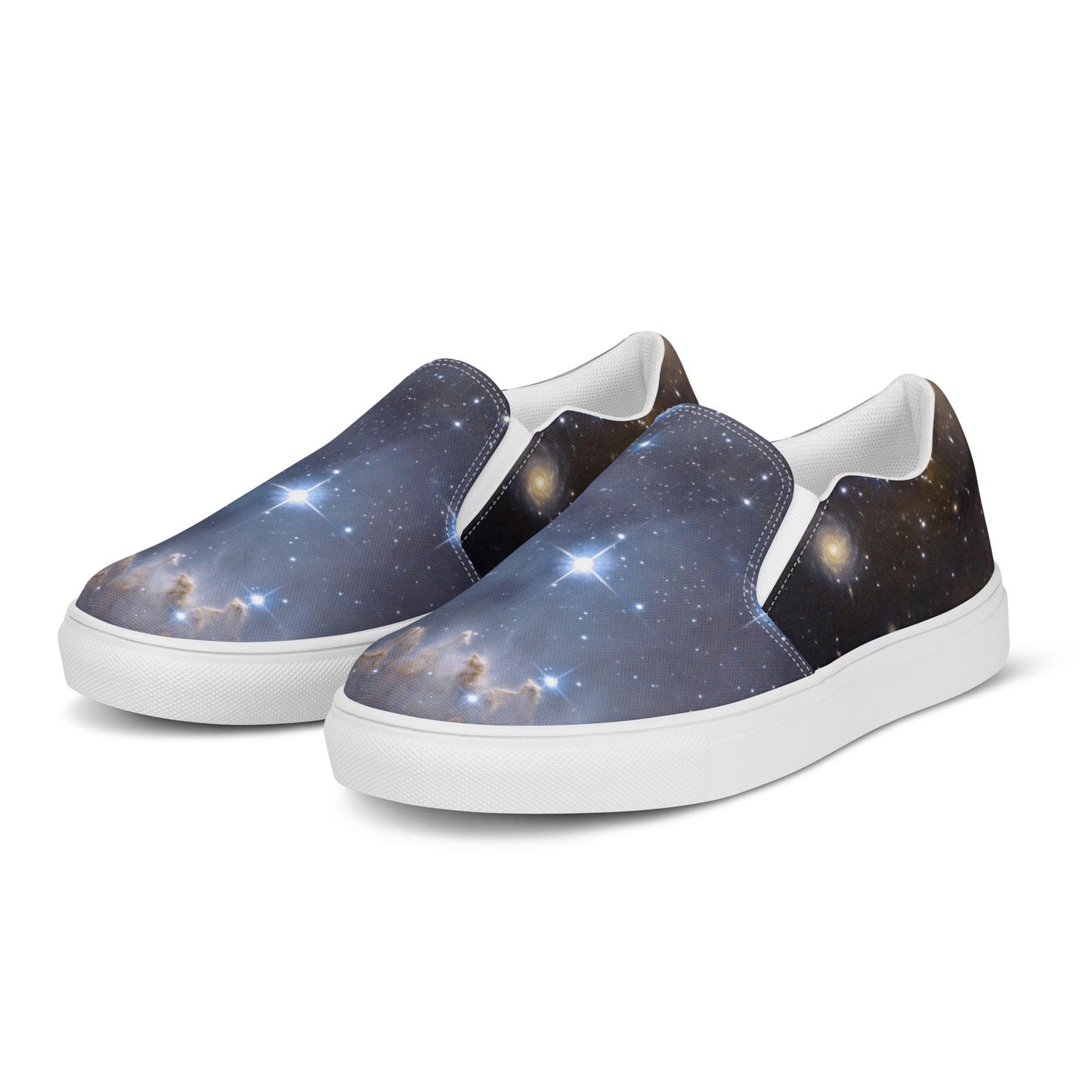 Pair of slip-on sneakers featuring a detailed galaxy print with bright stars, cosmic clouds, and nebulae in shades of blue, gold, and black. The shoes have white elastic side panels, white interiors, and white rubber soles, displayed on a clean white background.