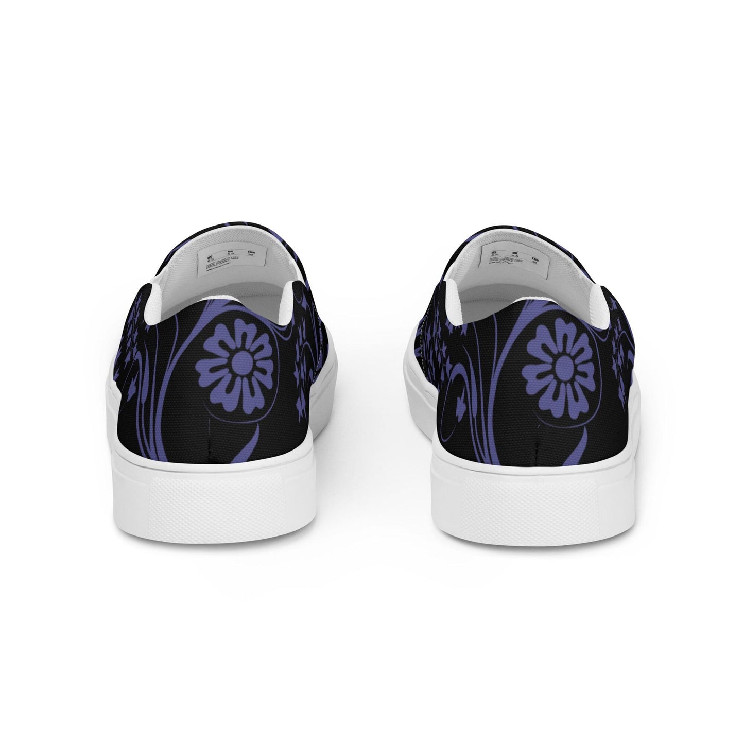 Back view of slip-on sneakers featuring a black canvas base with a decorative dark purple floral and vine design. The heels showcase a large stylized flower motif, and the shoes have white midsoles for a clean, modern contrast.