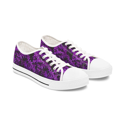 A pair of low-top sneakers is displayed on a white background. The shoes feature a vibrant purple floral pattern on a dark background. They have white laces, white rubber toe caps, and white soles with a black stripe, creating a crisp and stylish contrast with the bold floral design.
