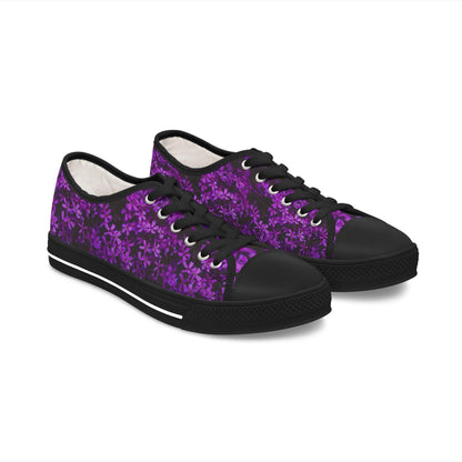 A pair of low-top sneakers is displayed on a white background. The shoes feature a vivid purple floral pattern on a dark background. They are designed with black laces, black rubber toe caps, and black soles with a white stripe, offering a bold contrast that highlights the rich floral design.