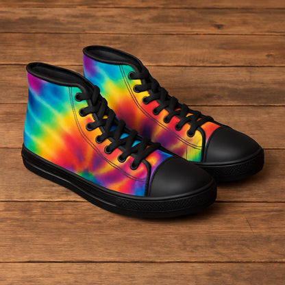 A pair of vibrant high-top sneakers is displayed on a wooden surface. The shoes feature a bold tie-dye pattern in bright shades of red, orange, yellow, green, blue, and purple. They have black laces, black rubber toe caps, and black soles, creating a striking contrast with the colorful design.