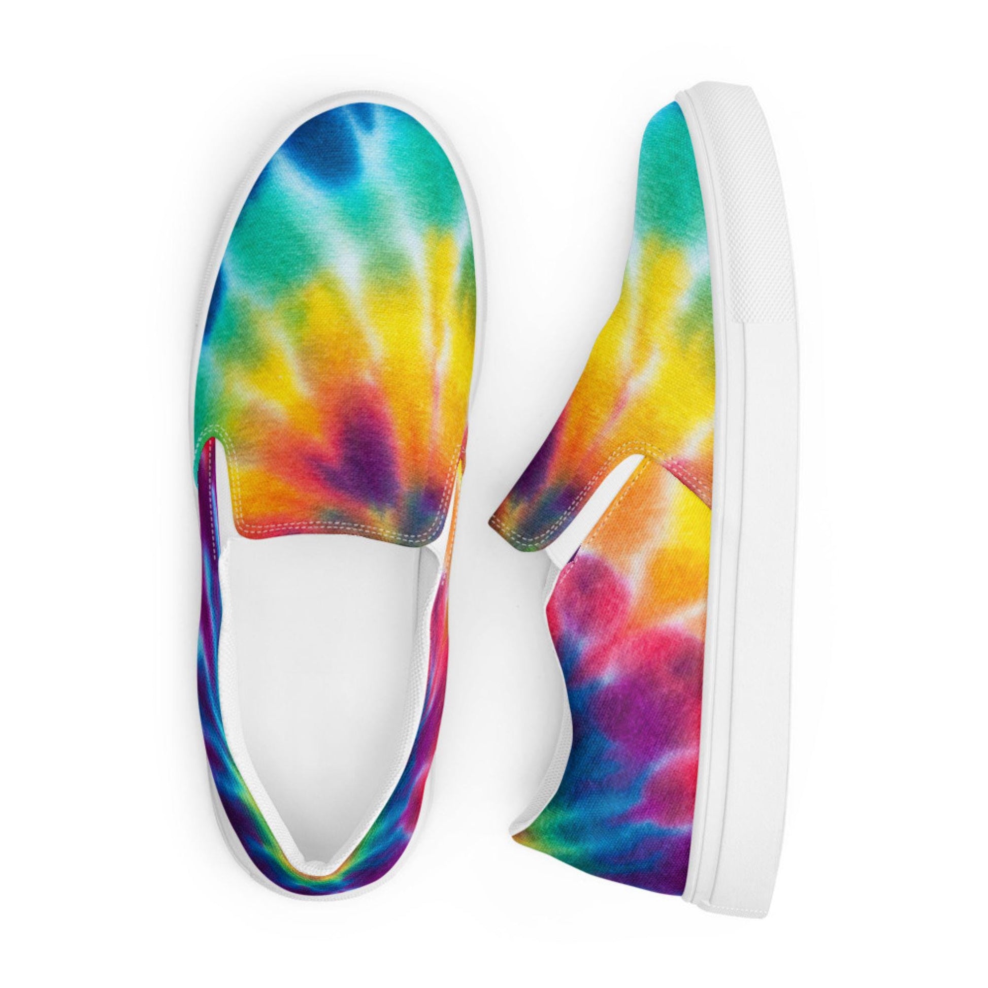 Top view of a pair of vibrant rainbow tie-dye slip-on canvas sneakers displayed on a white background. These colorful shoes feature a bold blend of turquoise, yellow, orange, red, purple, and blue in a swirling watercolor pattern. Designed with a crisp white rubber sole and elastic side accents for easy wear and all-day comfort.
