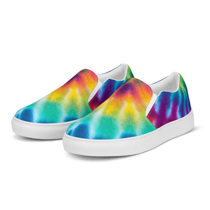 Front angled view of rainbow tie-dye slip-on canvas sneakers for women on a white background. These colorful casual shoes feature a bold blend of turquoise, aqua blue, yellow, orange, red, and purple in a smooth watercolor pattern. Built with a crisp white rubber sole and elastic side panels for easy wear and all-day comfort.