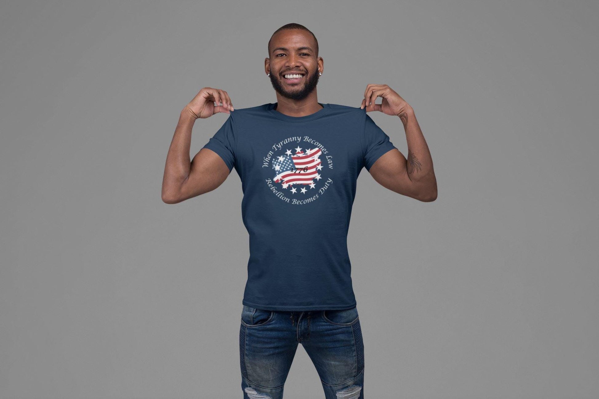 Smiling man wearing a blue graphic t-shirt featuring a distressed American flag with the quote &quot;When Tyranny Becomes Law, Rebellion Becomes Duty&quot; and the year 1776—patriotic apparel perfect for Independence Day or everyday freedom-loving style.