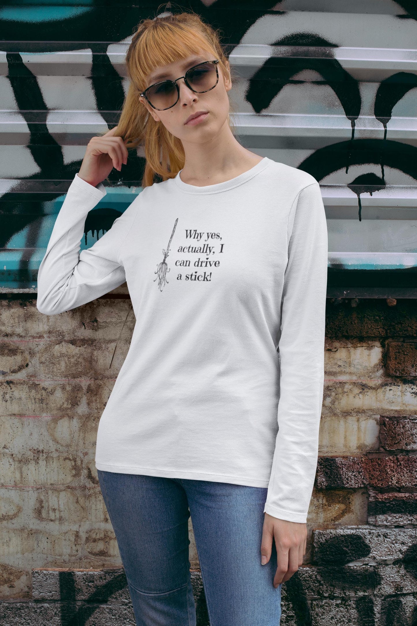 Woman wearing a white long-sleeve Halloween shirt featuring a black broomstick illustration and the humorous witch quote &quot;Why yes, actually, I can drive a stick!&quot; — perfect for spooky season style, witch-themed outfits, and fall festivities. Fun Halloween shirt for women, ideal for October parties, autumn layering, and casual witchcore fashion.
