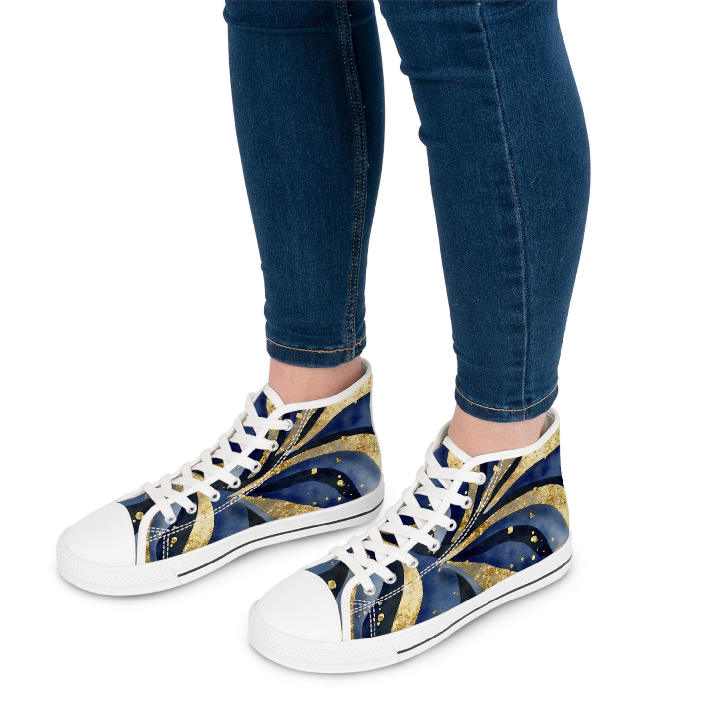 Close-up view of a person wearing high-top sneakers with a bold, artistic design featuring swirling navy blue, black, and gold patterns with dotted accents. The shoes have white laces, white soles, and are paired with dark blue skinny jeans. The background is plain white.