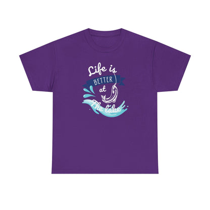 Flat lay of a purple unisex t-shirt featuring a graphic design with the phrase &#39;Life is Better at the Lake.&#39; The design includes a fish hook, water splash elements, and a navy blue banner, printed in white, blue, and aqua tones, on a plain white background.